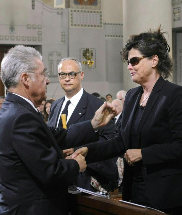 Eine Frau mit Sonnenbrille kondoliert einem Mann in einer Kirche.