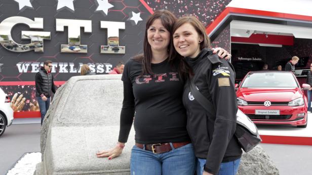 Zwei Frauen posieren vor einem GTI-Stand mit einem roten VW Golf im Hintergrund.