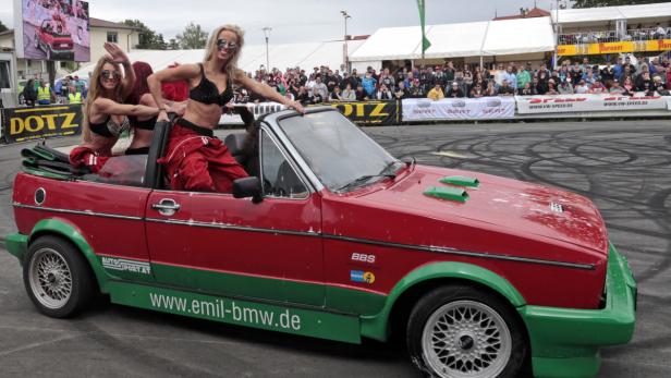 Zwei Frauen posieren in einem roten und grünen Cabriolet vor einer Zuschauermenge.