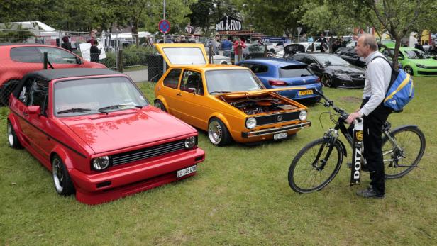 Ein Mann mit Fahrrad steht vor mehreren ausgestellten VW Golf Modellen.