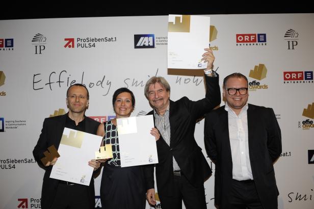 Vier Personen posieren mit goldenen Effie Awards vor einer Wand mit Logos.
