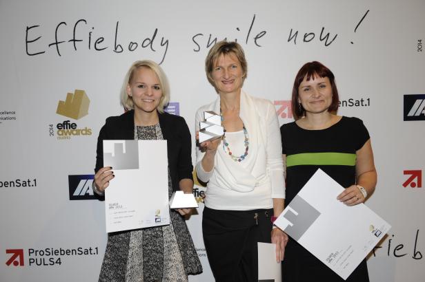 Drei Frauen posieren mit silbernen Effie Awards vor einer Wand mit dem Effie-Logo.