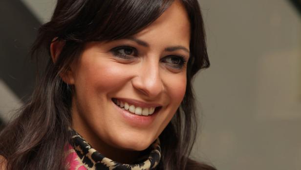 Eine lächelnde Frau mit dunklen Haaren und einem gemusterten Schal.