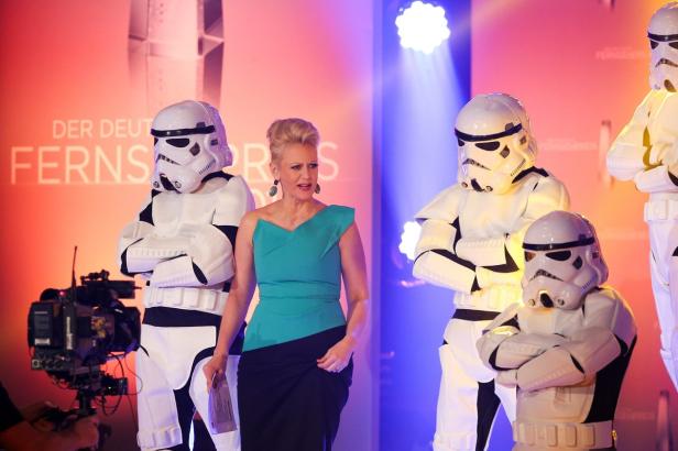 Eine Frau in einem türkisfarbenen Kleid steht neben als Stormtrooper verkleideten Personen.