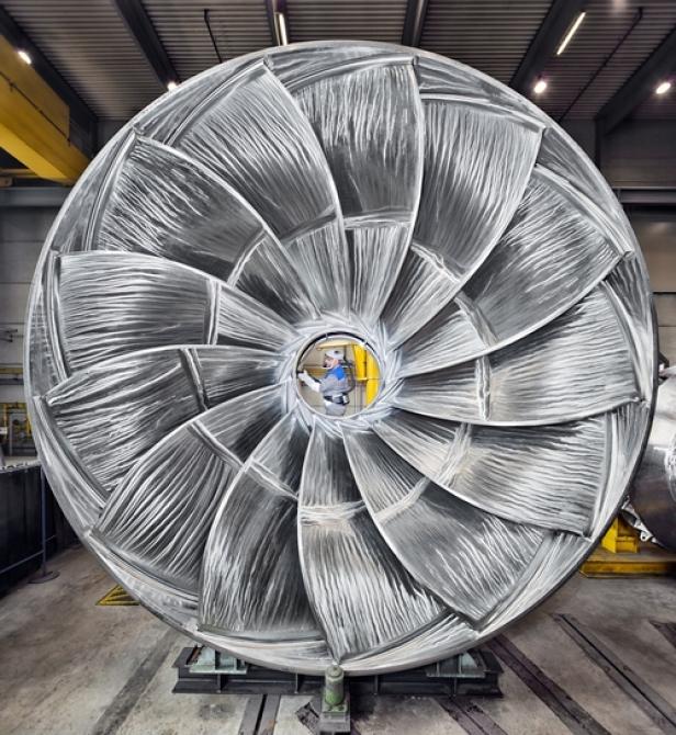 Ein Arbeiter inspiziert ein großes, silbernes Turbinenrad in einer Fabrikhalle.