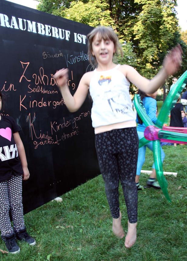Ein Mädchen springt barfuß vor einer Tafel, auf der Berufswünsche stehen.