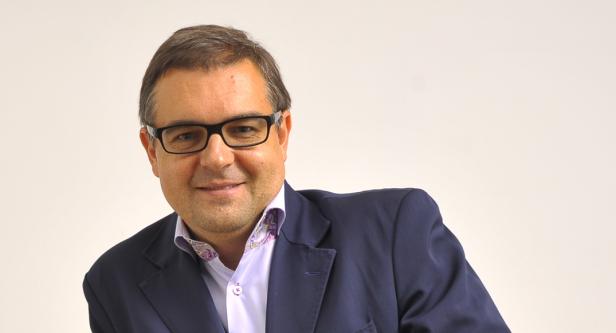Ein Mann mit Brille und blauem Sakko lächelt in die Kamera.