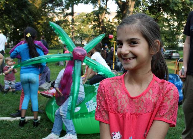 Ein lächelndes Mädchen steht vor einer Gruppe von Kindern auf einer Hüpfburg im Park.