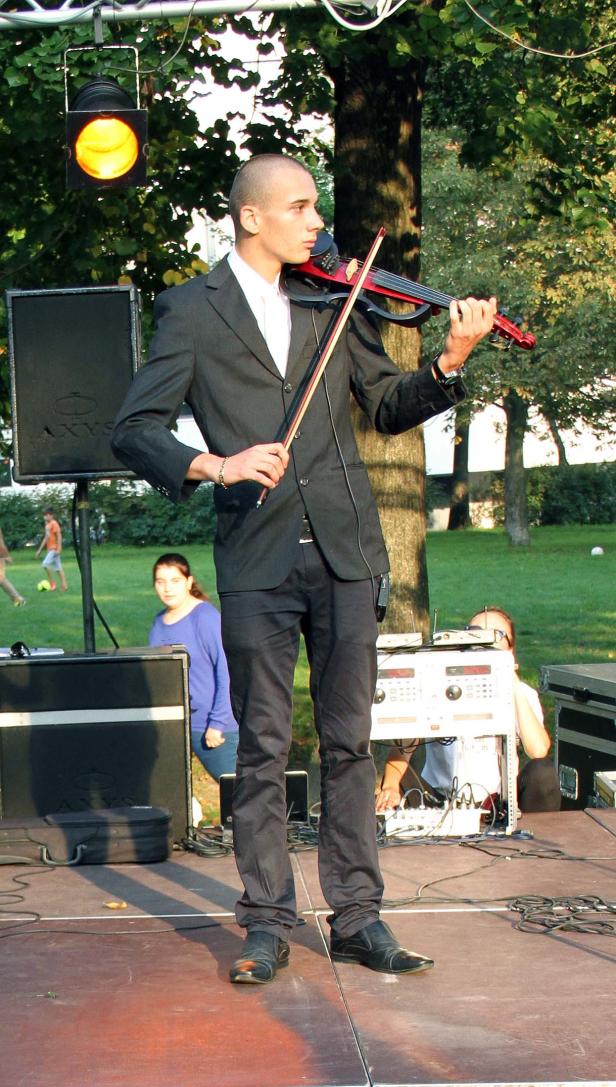 Ein Mann im Anzug spielt eine rote Geige auf einer Bühne.