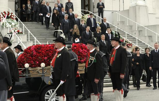 Ein Sarg, bedeckt mit roten Rosen, wird von Trauergästen begleitet.