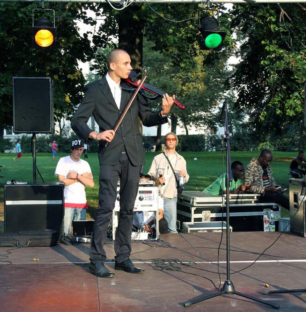 Ein Mann im Anzug spielt Geige auf einer Bühne vor Publikum.