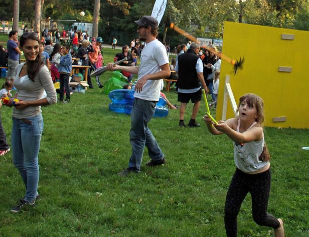 Auf einer Wiese spielen Menschen mit Jonglierkeulen und einem Katapultspiel.