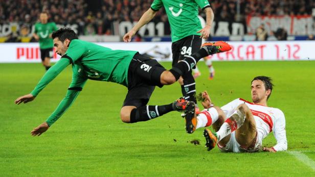 Ein Fußballspieler in Grün grätscht einen Spieler in Weiß ab, wobei Gras aufwirbelt.