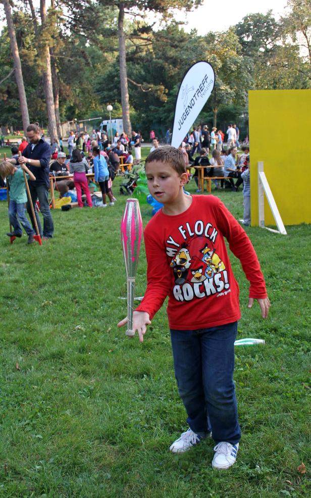 Ein Junge jongliert mit einem Diabolo auf einer Wiese.