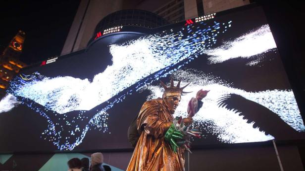 Eine lebende Statue der Freiheitsstatue steht vor einer großen LED-Wand in New York.