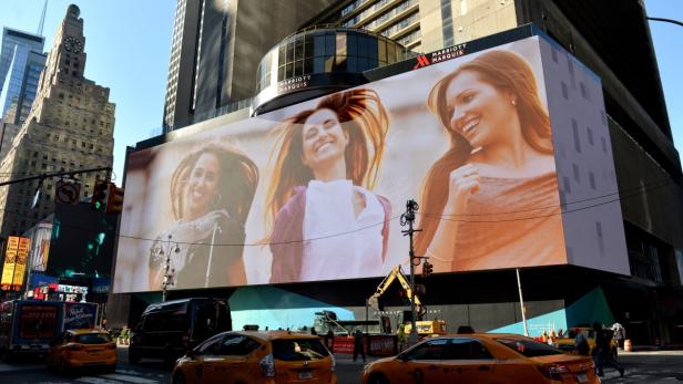 Ein großes Werbeplakat mit drei lächelnden Frauen am Times Square in New York.