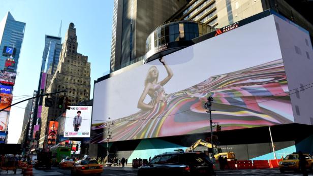 Ein großes Werbeplakat mit einer Frau in einem bunten Kleid am Times Square, New York.