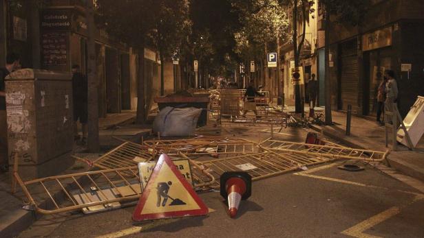 Eine Straße ist mit umgestürzten Bauzäunen und einem Warnschild blockiert.