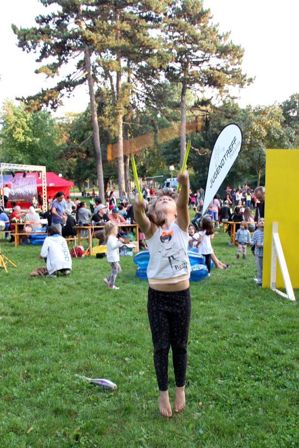 Ein junges Mädchen jongliert auf einer Wiese mit gelben Stäben.