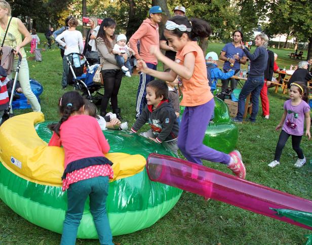 Kinder spielen auf einer Hüpfburg und einer Wippe im Freien.