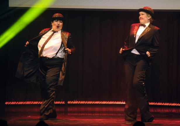 Zwei Performer in Anzügen und Hüten stehen auf einer Bühne.