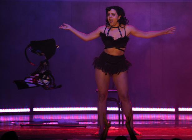 Eine Frau in einem schwarzen Burlesque-Outfit wirft einen Hut in die Luft.