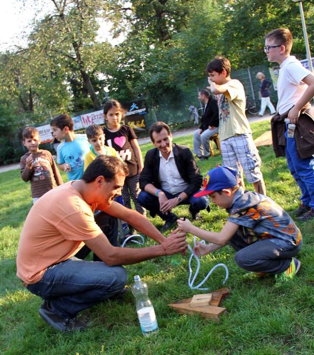 Ein Mann zeigt einem Kind im Freien einen Trick mit einer Schnur.