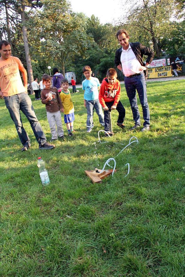 Eine Gruppe von Kindern und Erwachsenen beim Starten einer Wasserrakete im Park.