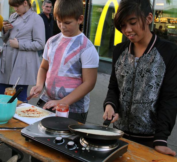 Zwei Jugendliche bereiten Crêpes auf einem Tisch vor einem McDonald’s zu.