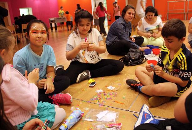 Eine Gruppe Kinder sitzt auf dem Boden und bastelt mit bunten Gummibändern.
