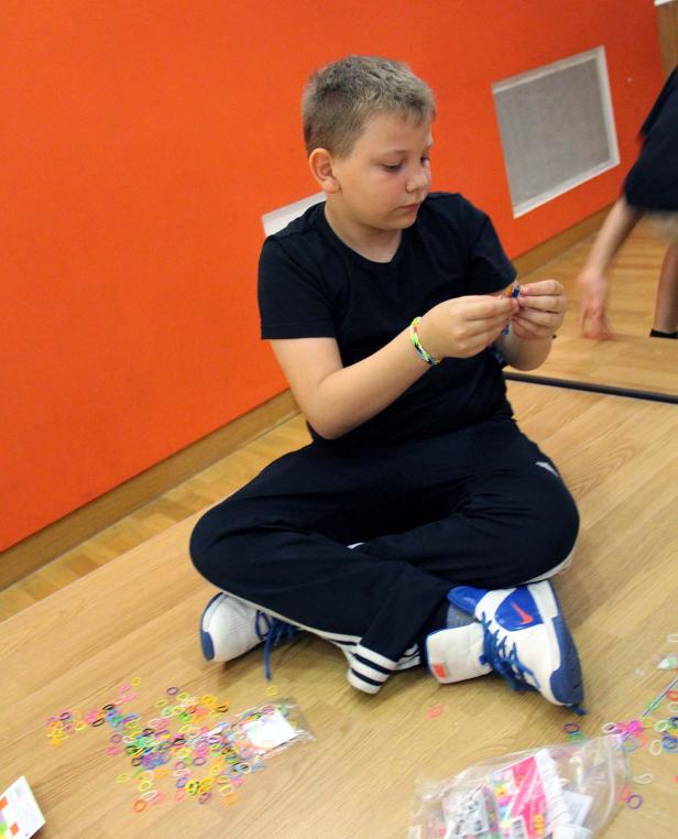 Ein Junge sitzt auf dem Boden und bastelt mit bunten Gummibändern.