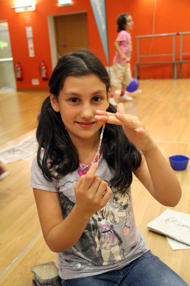 Ein Mädchen sitzt auf dem Boden und macht eine Kette aus Gummibändern.