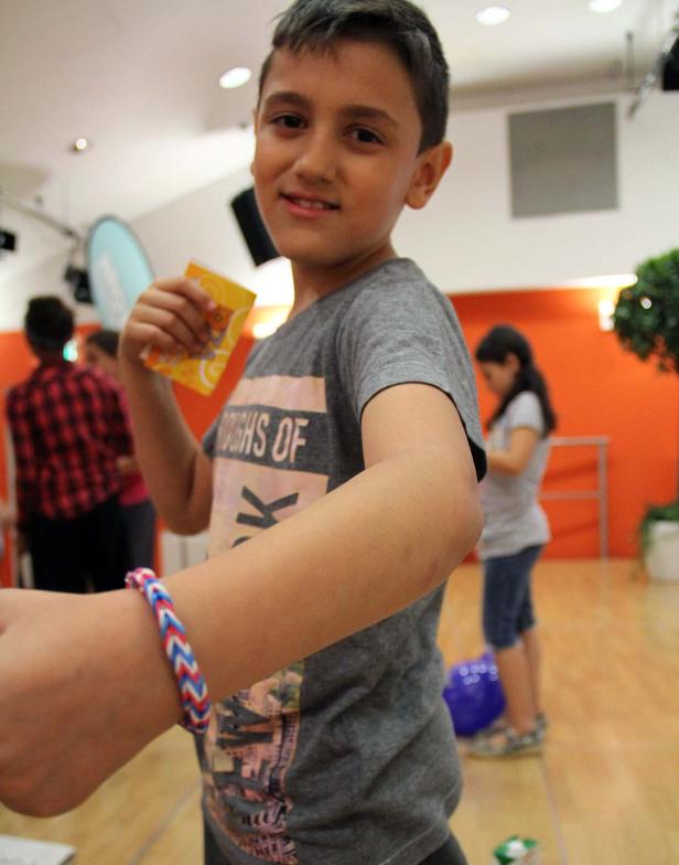 Ein lächelnder Junge mit einem bunten Armband hält eine kleine gelbe Packung in der Hand.
