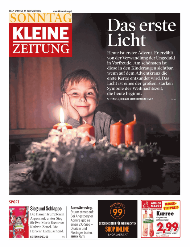 Ein Kind betrachtet lächelnd die erste brennende Kerze auf dem Adventskranz.