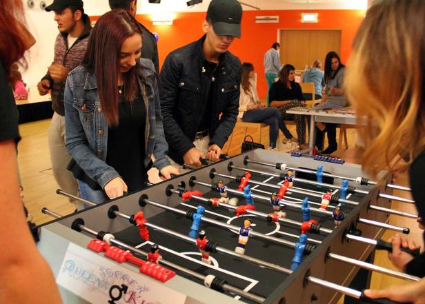 Mehrere Personen spielen Tischfußball in einem Innenraum.