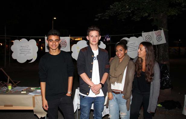 Vier junge Leute stehen lächelnd vor einem Stand mit der Frage nach der Jugendarbeitslosenquote.