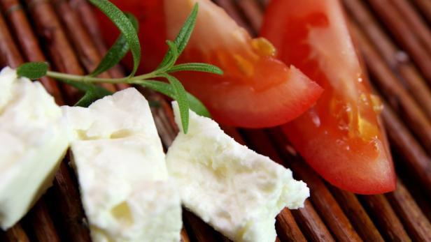 Feta-Käsewürfel, Tomatenspalten und Rosmarin auf einem Holztablett.