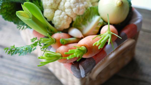 Ein Korb gefüllt mit frischem Gemüse wie Karotten, Lauch, Blumenkohl und Zwiebeln.