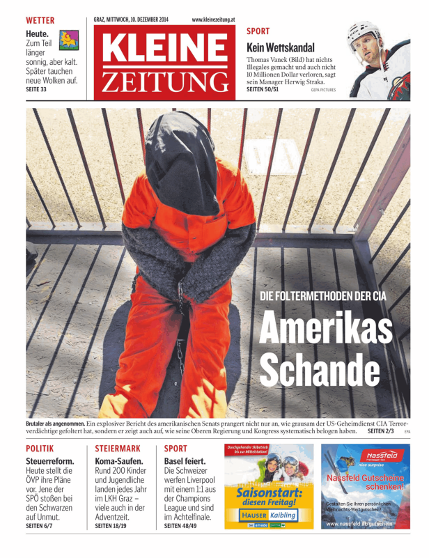 Eine gefesselte Person in orangefarbener Kleidung steht hinter einem Gitter.
