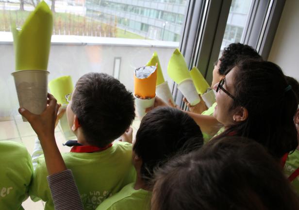 Eine Gruppe von Kindern hält selbstgebastelte Raketen aus Bechern und Papier in die Höhe.