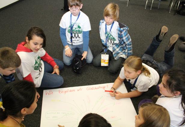 Eine Gruppe Kinder sitzt um ein Plakat und diskutiert über Klimaschutz.