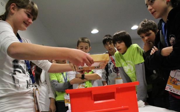 Eine Gruppe von Kindern beobachtet, wie ein Mädchen Wasser durch einen Rahmen in einen roten Behälter gießt.