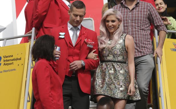 Ein Mann im roten Anzug führt eine Frau mit rosa Haaren am Vienna International Airport ab.