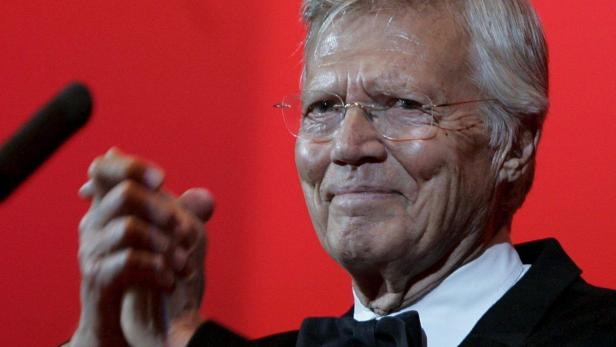 Schauspieler Hardy Krüger lächelt vor einem roten Hintergrund.