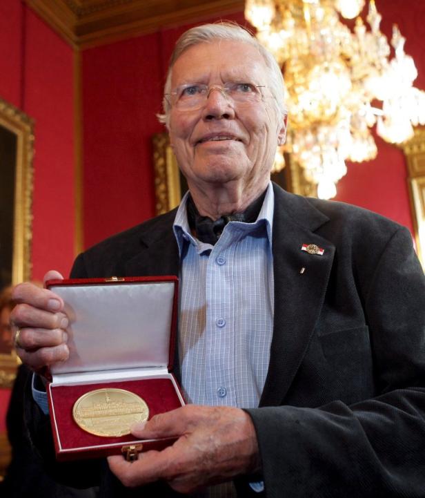 Ein älterer Mann hält eine Medaille in einer roten Schatulle.