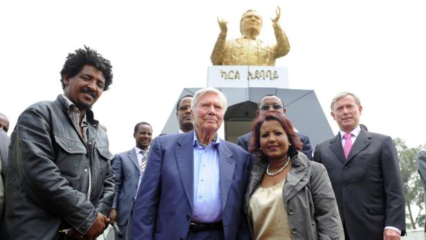 Eine Gruppe von Menschen steht vor einem Denkmal mit einer goldenen Statue.