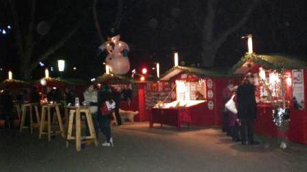 Ein Weihnachtsmarkt mit roten Buden und einem aufblasbaren Schneemann im Dunkeln.