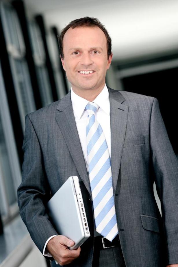 Ein Mann im Anzug hält einen Laptop in der Hand.