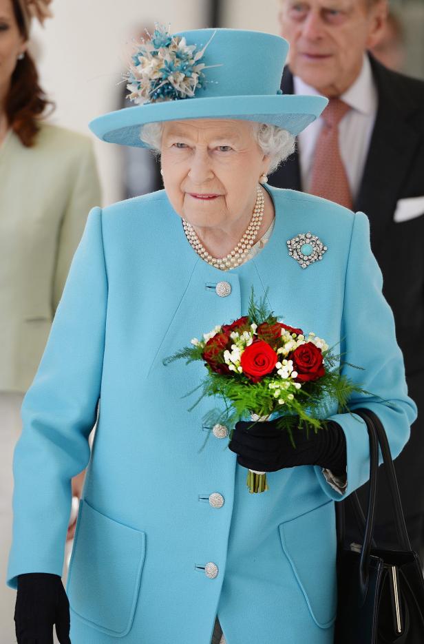 Königin Elisabeth II. in einem hellblauen Kostüm mit einem Blumenstrauß in der Hand.