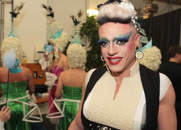 Eine Dragqueen mit auffälligem Make-up und historisch inspiriertem Kostüm lächelt.